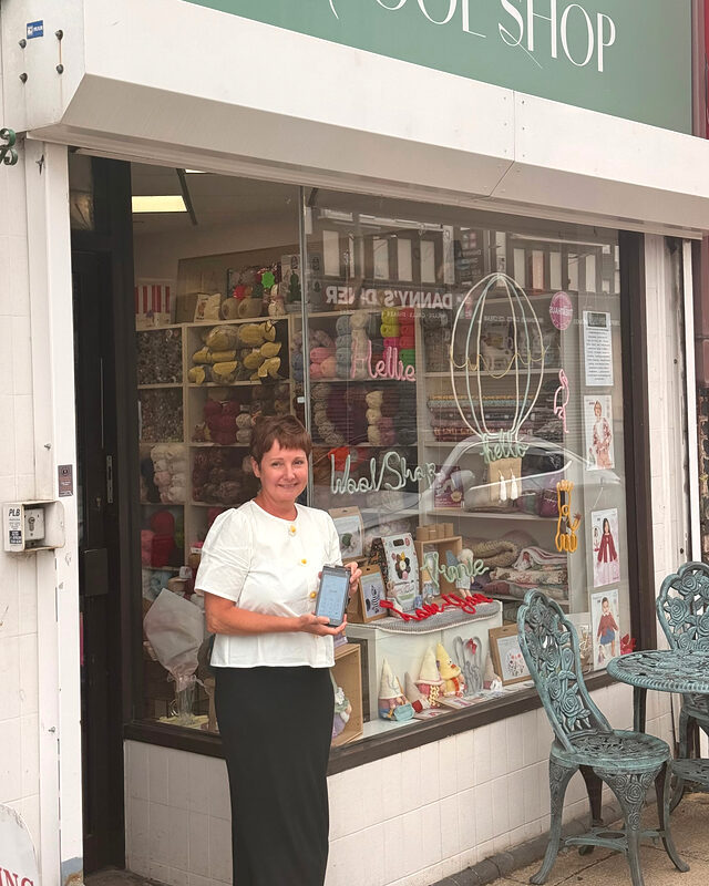 Wool shop owner in Dinnington outside her shop holding a Shift4 card machine